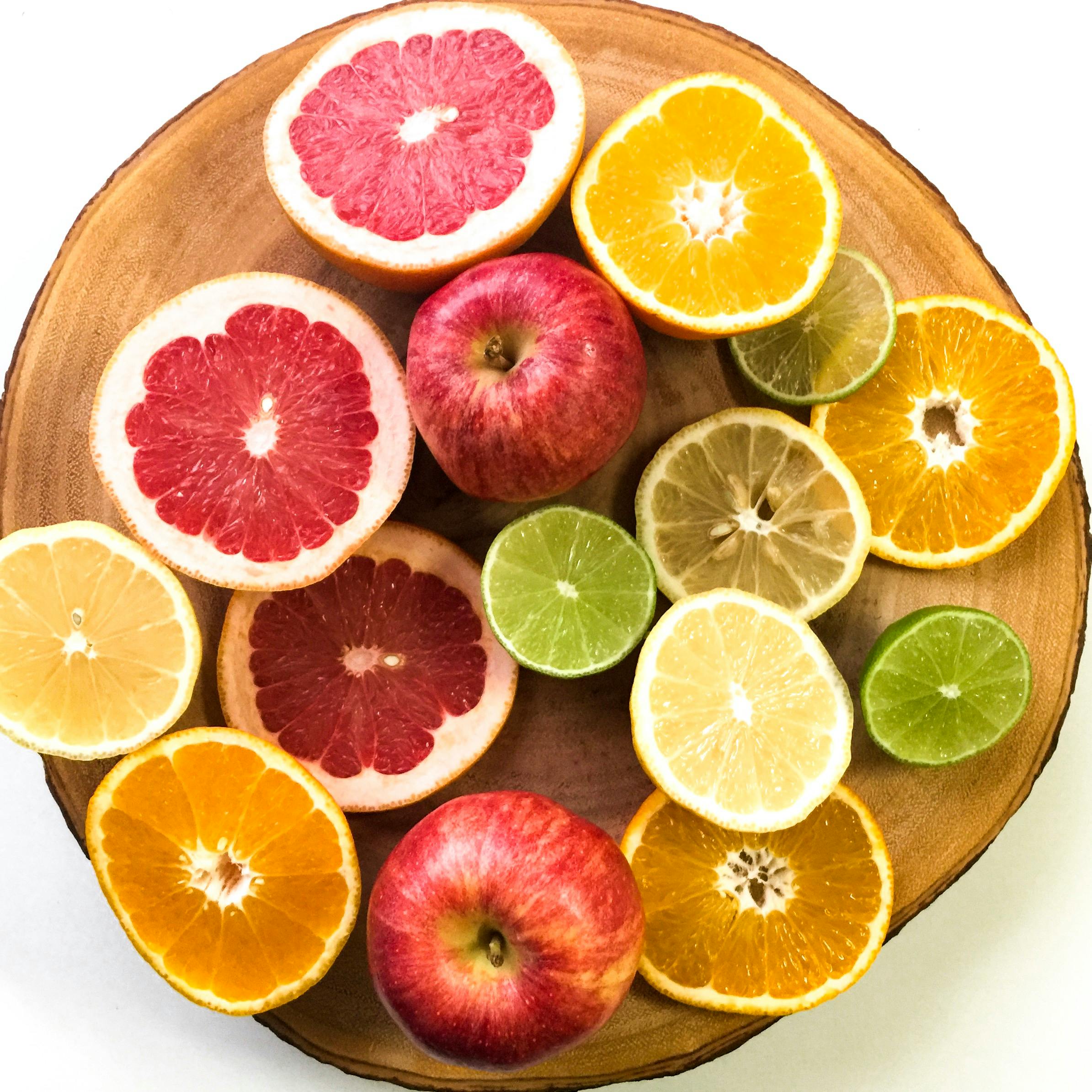 Vibrant display of sliced citrus fruits and apples on a wooden platter, emphasizing freshness and healthy eating.