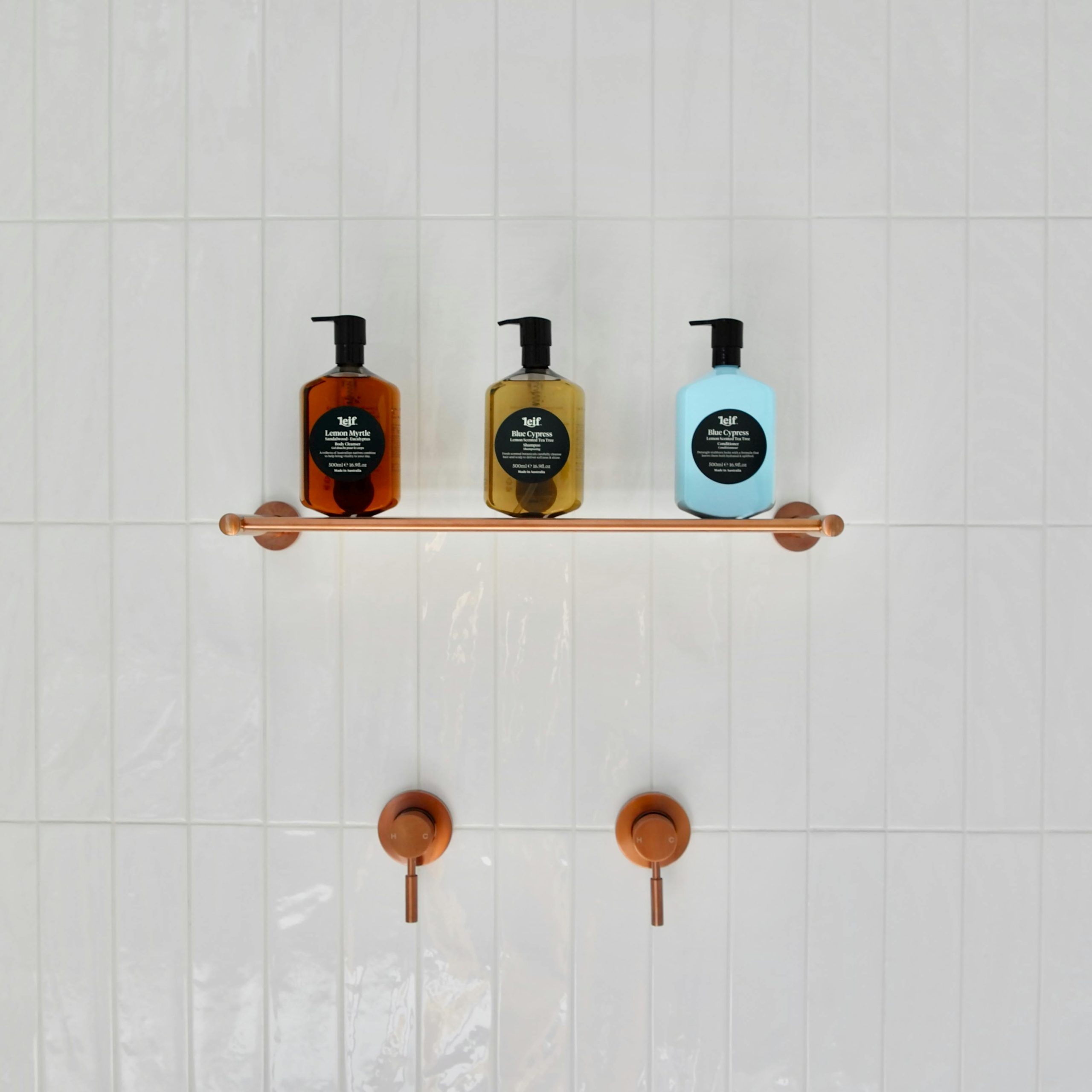 A minimalist bathroom shelf showcasing three hygiene product dispensers on a tiled wall.