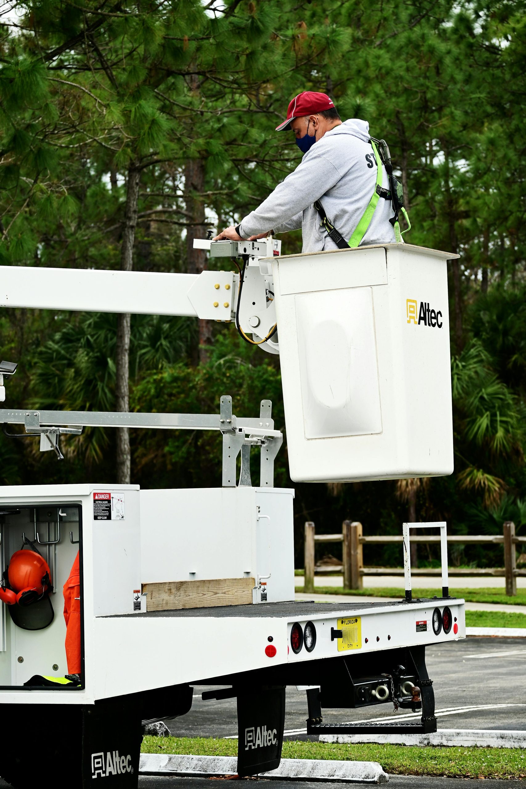 Construction worker in safety gear operates a bucket truck for outdoor maintenance task.