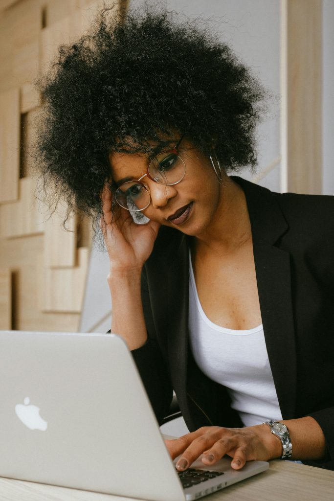 Businesswoman with afro hairstyle working on a laptop, looking focused and professional in an office setting.